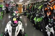 A snowmobile sitting in a showroom with clothing hanging on the walls around it